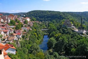 A scenic town nestled by a river, surrounded by lush trees.