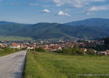 A winding road leading to a picturesque mountain village, surrounded by lush greenery and towering peaks.