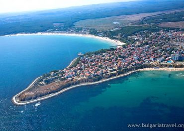 Aerial view of a quaint coastal town with colorful buildings, sandy beaches, and boats in the harbor.