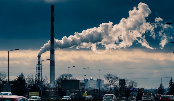 Smoke from factory can be seen in background, cars on the road in the foreground