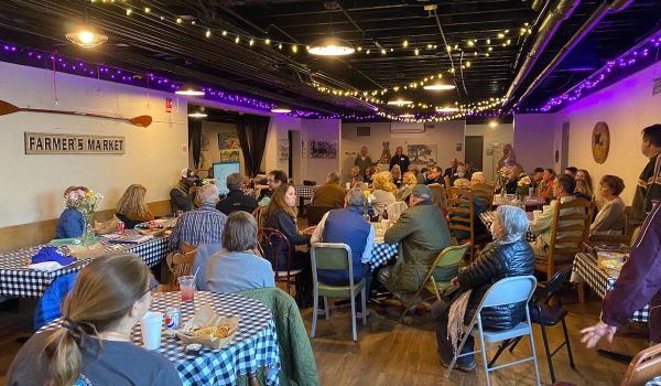 People sit at tables in a room with string lights hanging from the ceiling