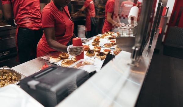 Fast food workers preparing meals. They're all wearing red t-shirts.