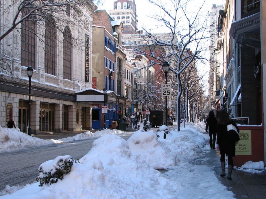 People walk on the sidewalk across from Forrest Theatre; there snow on the road and sidewalk