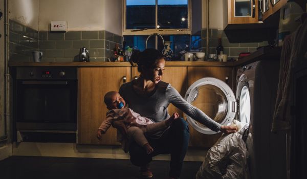 Mom struggling to do laundry with baby.