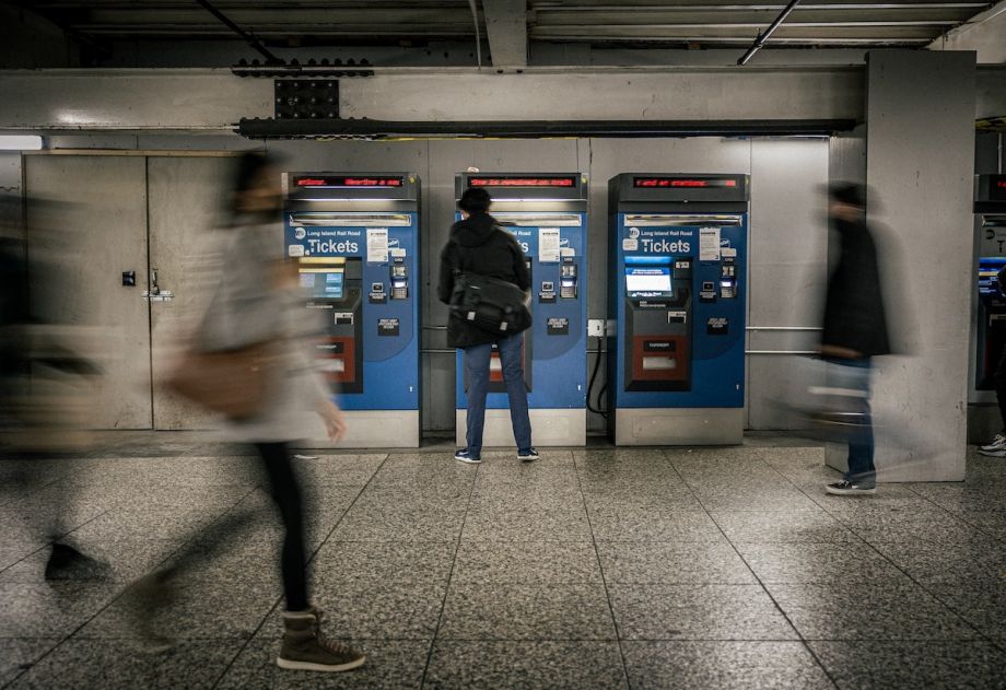 Person buys ticket at Metrocard kiosk; other people are blurred walking behind them