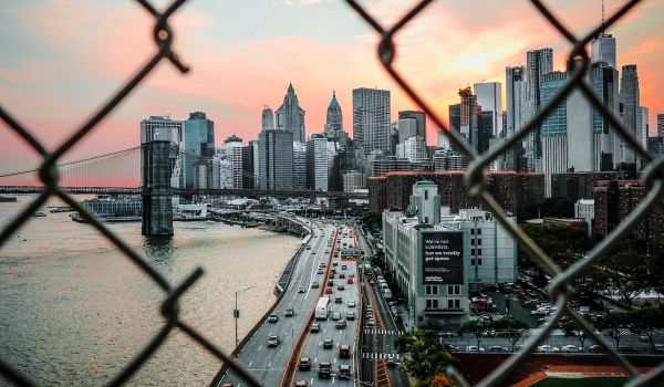 Looking through a gate toward lower Manhattan in New York City. Cars driving on the highway and skyscrapers.