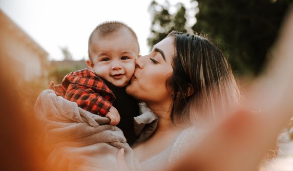 Person kisses baby on cheek while taking picture