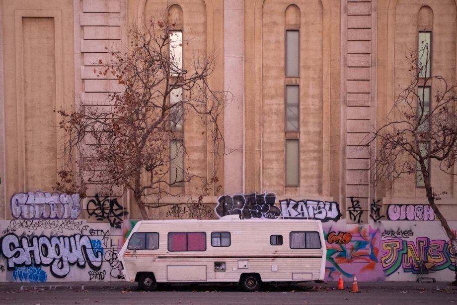 RV parked on a street with wall tagged with graffiti in the background