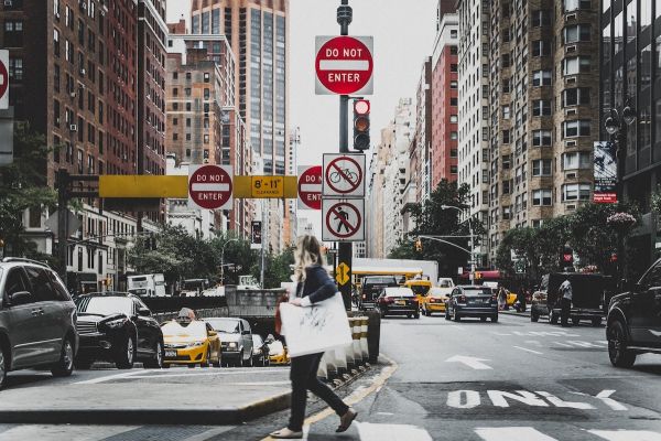 Person walks in a crosswalk in New York City. Cars and traffic signs can be seen in background.